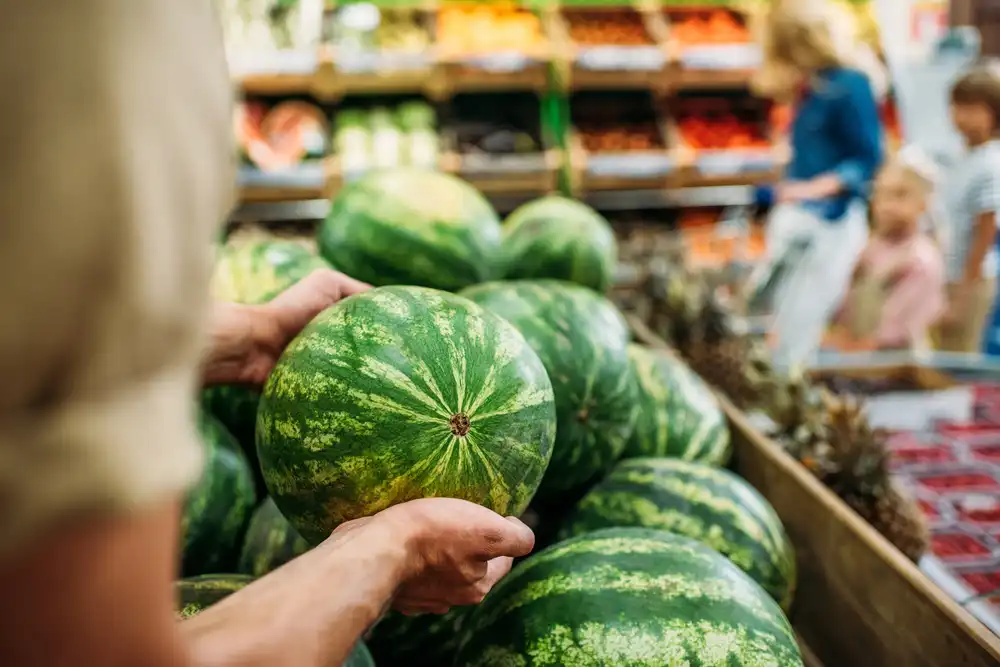 Zákazník vyberajúci melón v supermarkete medzi ďalšími čerstvými plodmi.