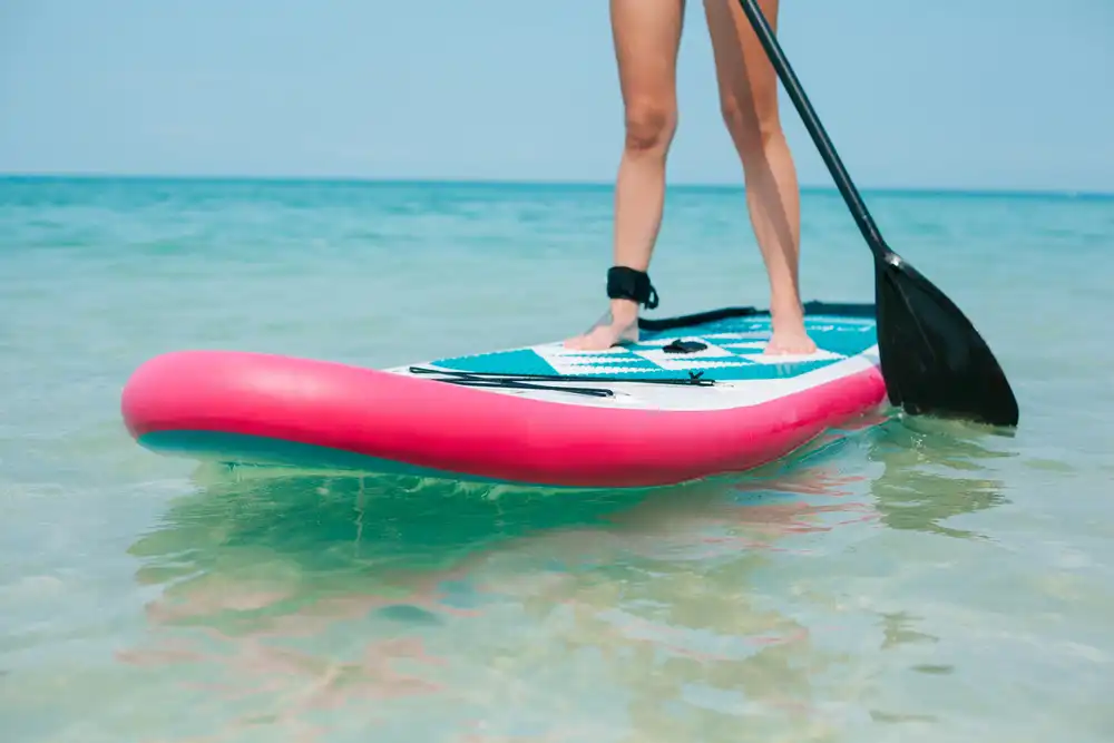 Žena stojaca na paddleboarde s ružovým pruhom na mori, ukážka univerzálneho allround paddleboardu.