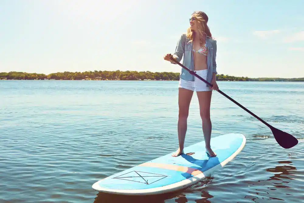 Žena stojaca na paddleboarde s veslom na pokojnej vode, ideálne pre rekreačný paddleboarding.