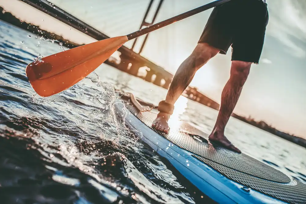 Detailný záber vesla a nôh na paddleboarde, zachytenie dynamiky pri jazde.