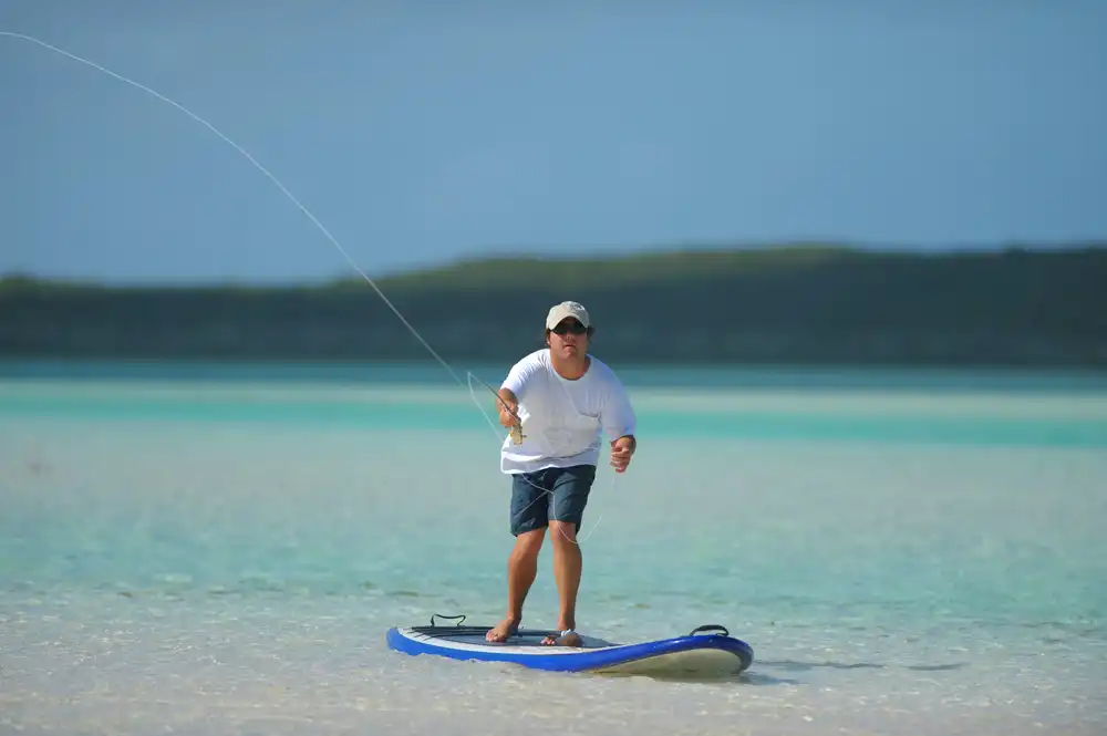 Muž loviaci ryby na paddleboarde v plytkej tyrkysovej vode, ukážka paddleboardu na rybolov.