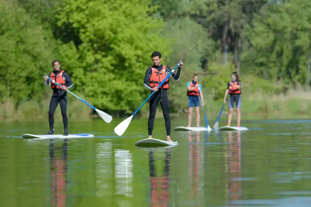 Skupina ľudí na paddleboardoch na pokojnej rieke, príklad touring paddleboardov pre dlhšie trasy.