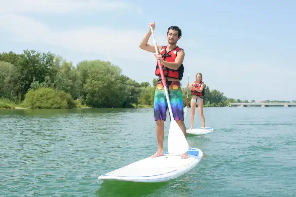 Muž a žena na paddleboardoch s veslami na pokojnej rieke, vhodné pre rodinné výlety.