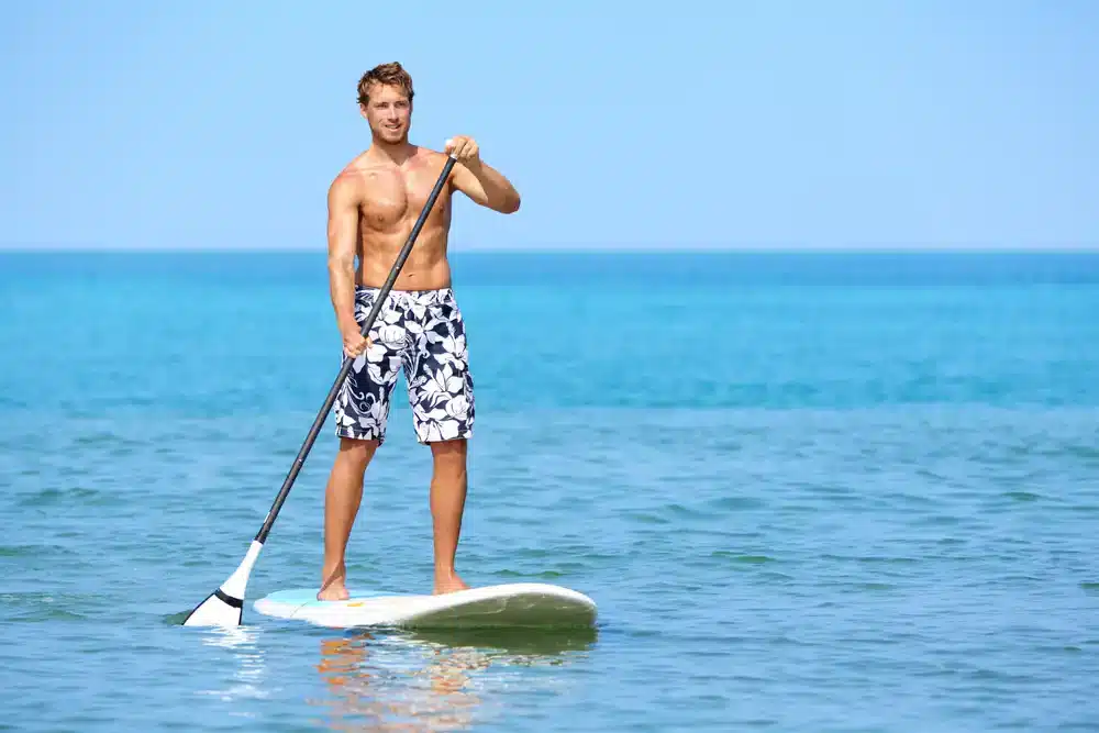 Muž veslujúci na paddleboarde v mori, vhodné pre športové aj rekreačné využitie.