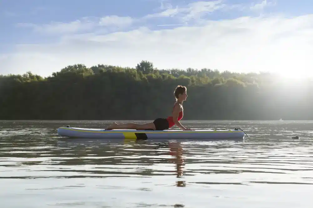 Žena cvičiaca jogu na paddleboarde pri východe slnka, paddleboardy vhodné na jogu.